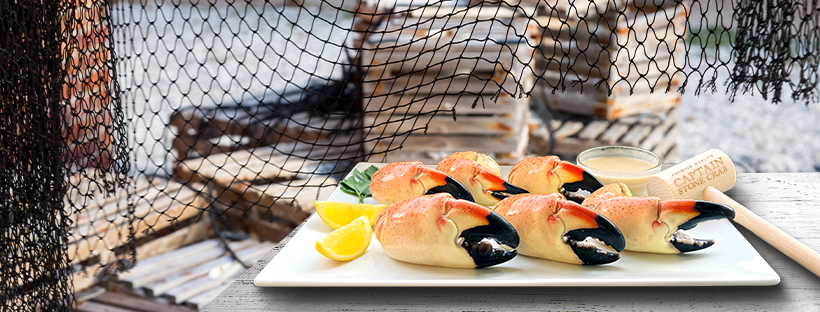 Crab claws in a white platter and a dip and wedge of lemon. it also has a small wooden mallet.