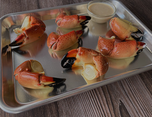 Cooked stone crab claws on a metal tray with sauce and lemon wedge.