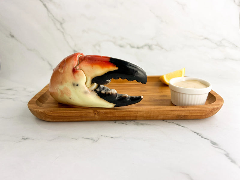 Cooked stone crab claw on a wooden tray with lemon wedge and dipping sauce.
